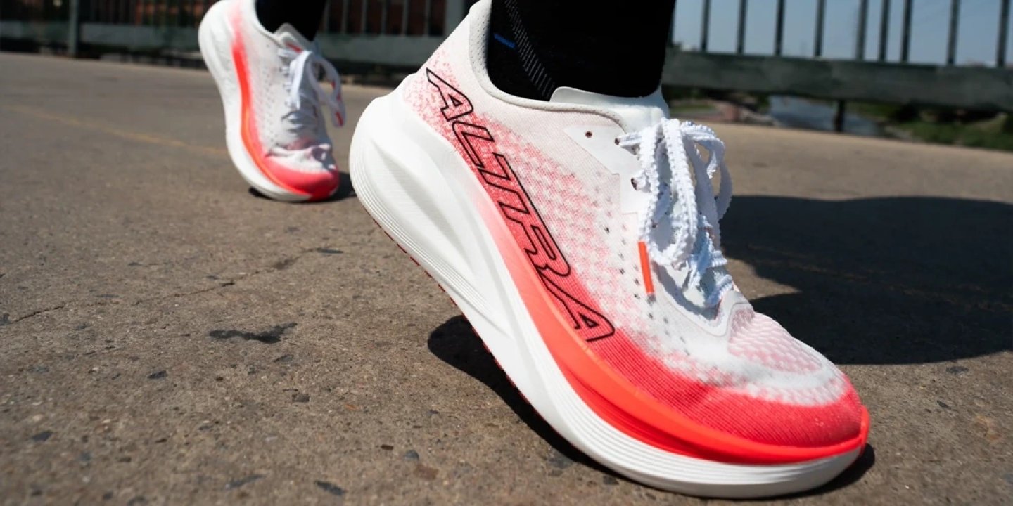 Altra Vanish Tempo 2 running shoes in white and coral colorway worn on asphalt pavement, close-up side view.
