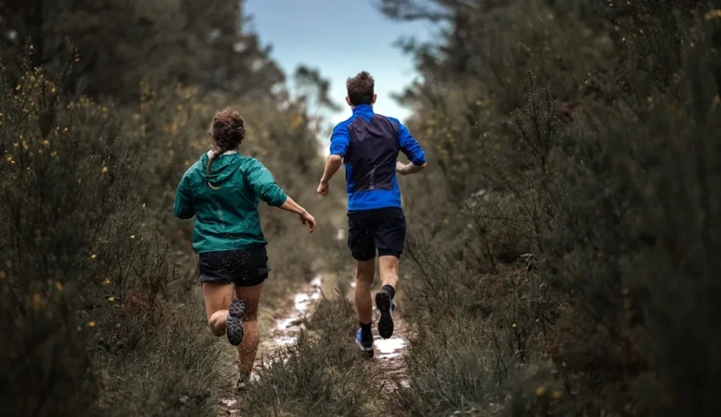 Two trail runners from behind on a narrow muddy forest path wearing Salomon running jackets and shorts