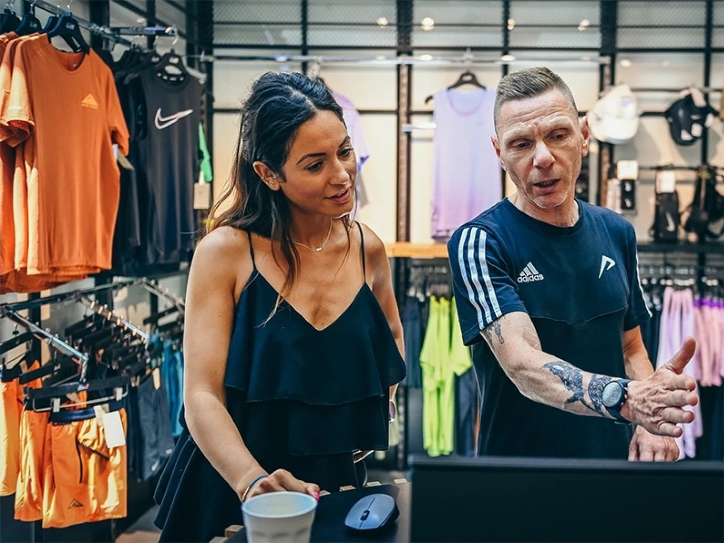 Male running specialist in Adidas shirt advising a female customer at a computer in a running apparel retail store.