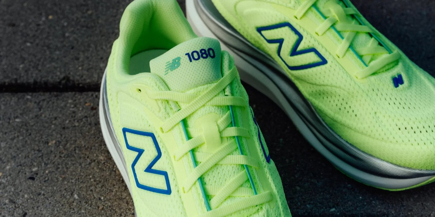 New Balance 1080 running shoes in neon yellow with blue NB logo, shown close up on a grey paved surface.