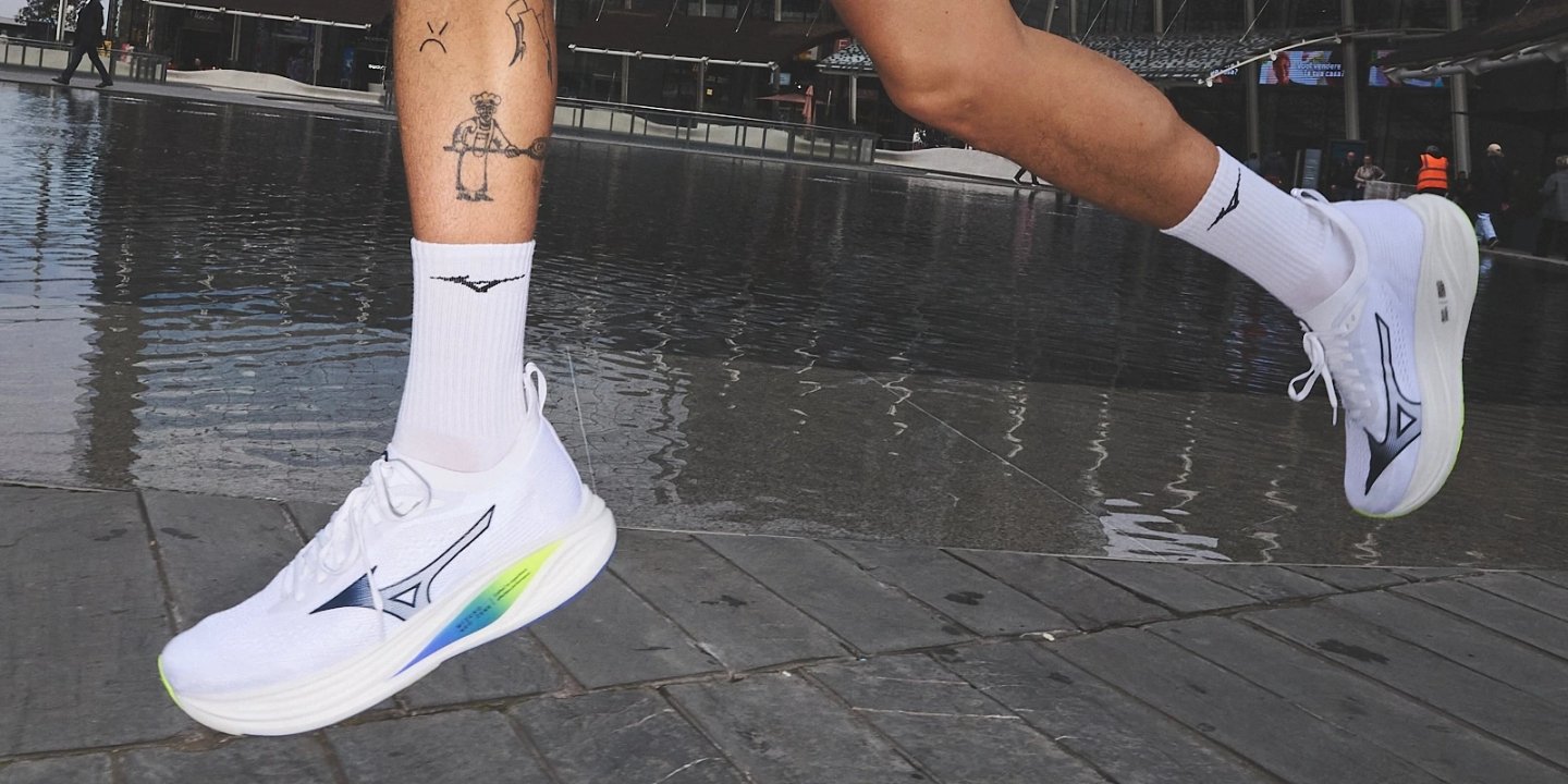 Runner wearing white Mizuno Neo Wind running shoes with rainbow gradient midsole on wet urban pavement