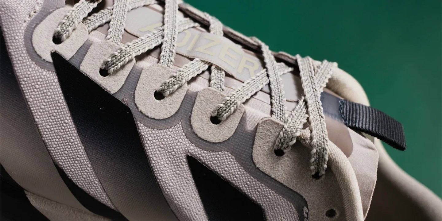 Close-up of Adidas Adizero running shoe showing lace-up detail, textured upper, three stripes, and black heel tab.