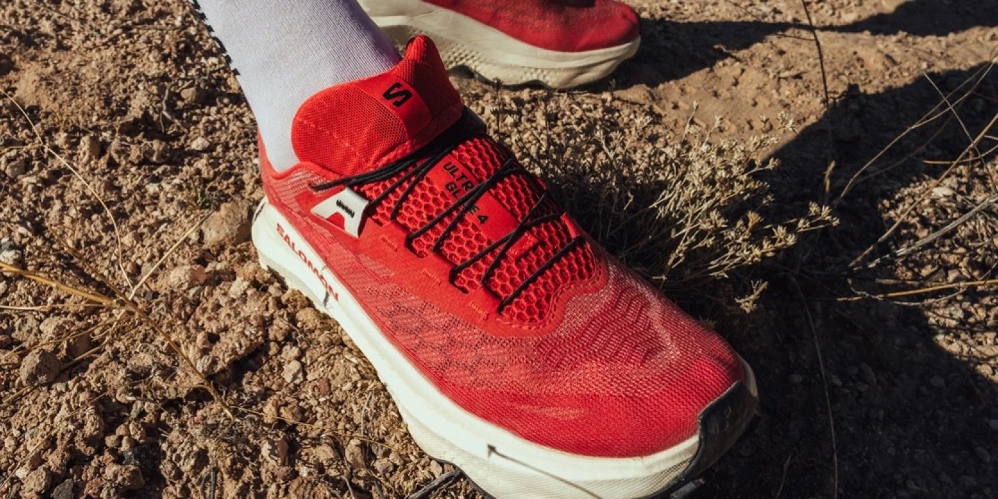 Red Salomon Ultra Glide 4 trail running shoe worn on dry rocky desert trail with white compression socks