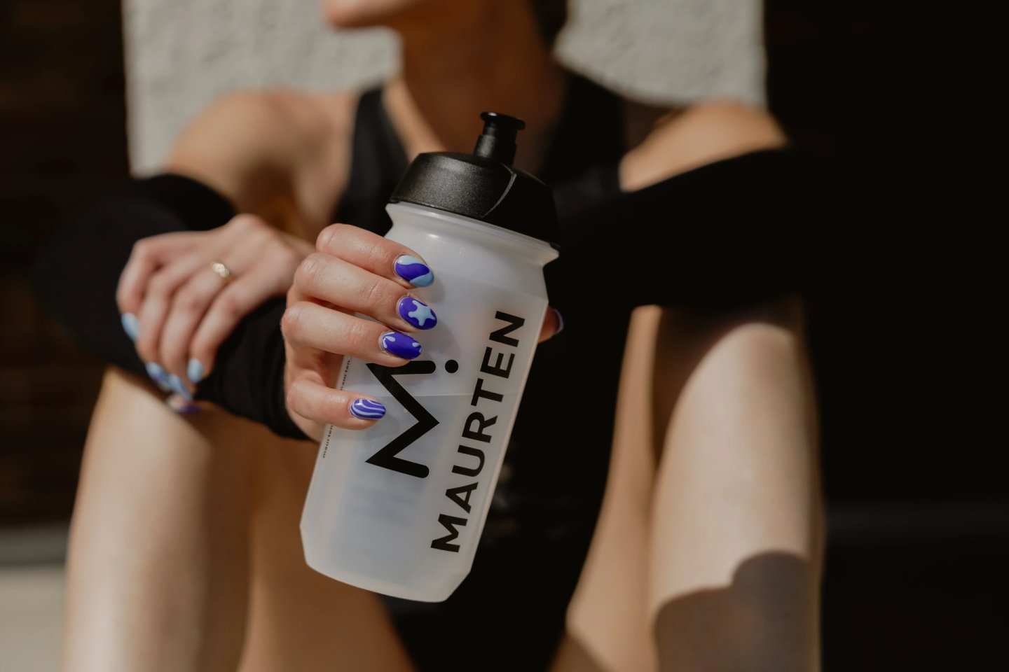 Woman holding a frosted clear Maurten branded sports water bottle with black push-pull cap