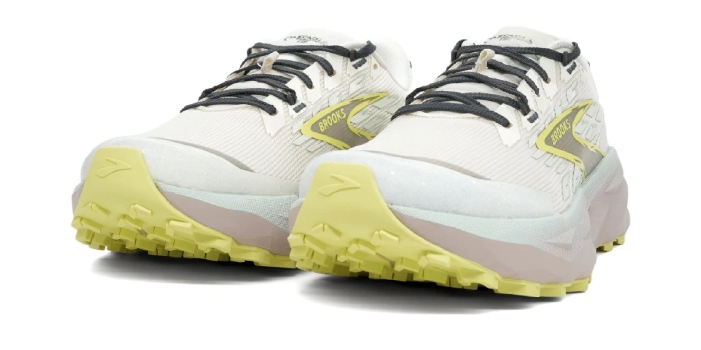 Pair of Brooks trail running shoes in white with lime yellow outsole lugs and dark grey laces, front three-quarter view