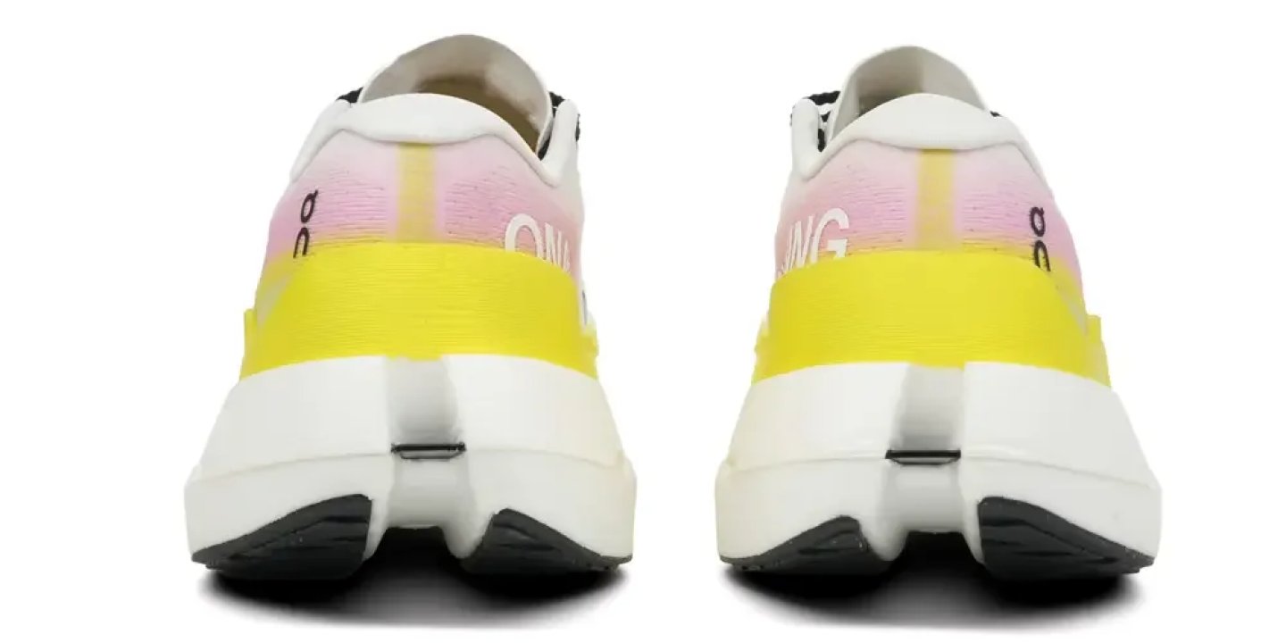Rear view of On Running shoes with pink gradient upper, yellow heel stripe, white midsole, and black outsole.