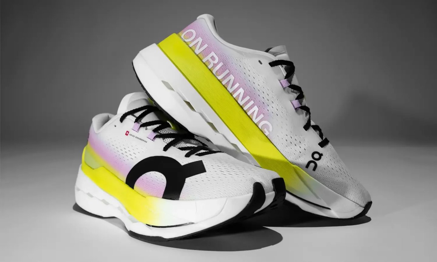 Pair of On Running trainers with white mesh upper, pink-yellow gradient, neon yellow midsole stripe, and black On logo.