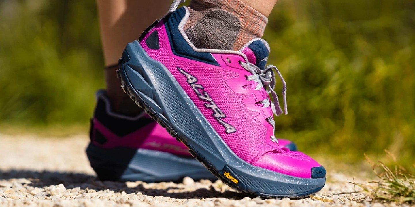 Women's Altra trail running shoe in pink and navy with Vibram outsole on gravel trail path outdoors