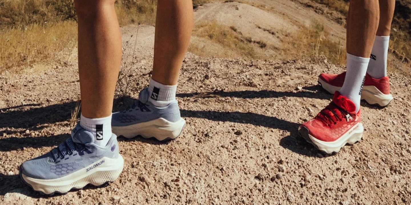 Two runners wearing Salomon trail running shoes in blue and red on a dry rocky desert trail path