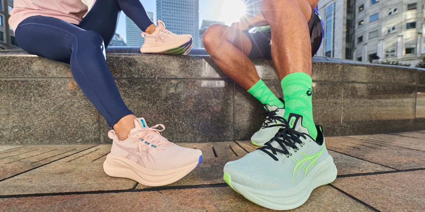 Man and woman wearing ASICS running shoes seated on urban steps, womens pink and mens mint green colorways