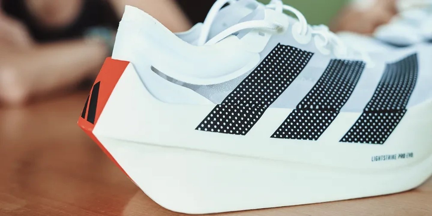 Adidas Adizero Adios Pro running shoe in white with black three stripes and orange heel accent.