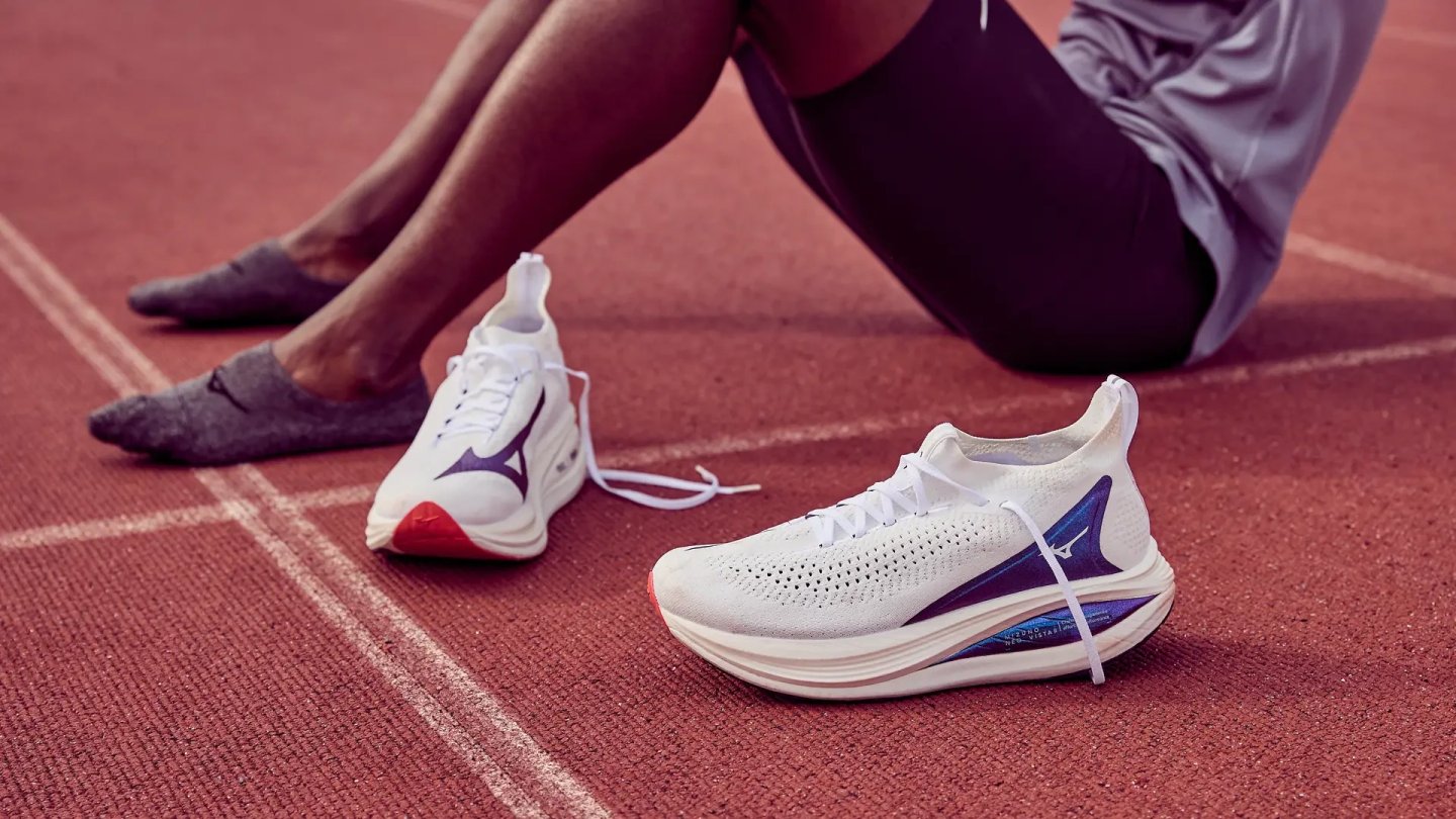 Pair of Mizuno Neo Vista running shoes in white and blue on a red athletics track with a seated athlete