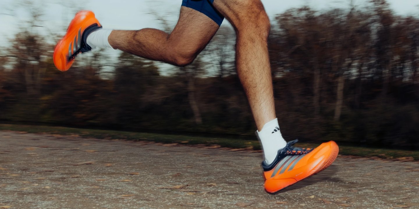 Male runner in motion wearing adidas orange and navy racing shoes with white adidas ankle socks on a paved path