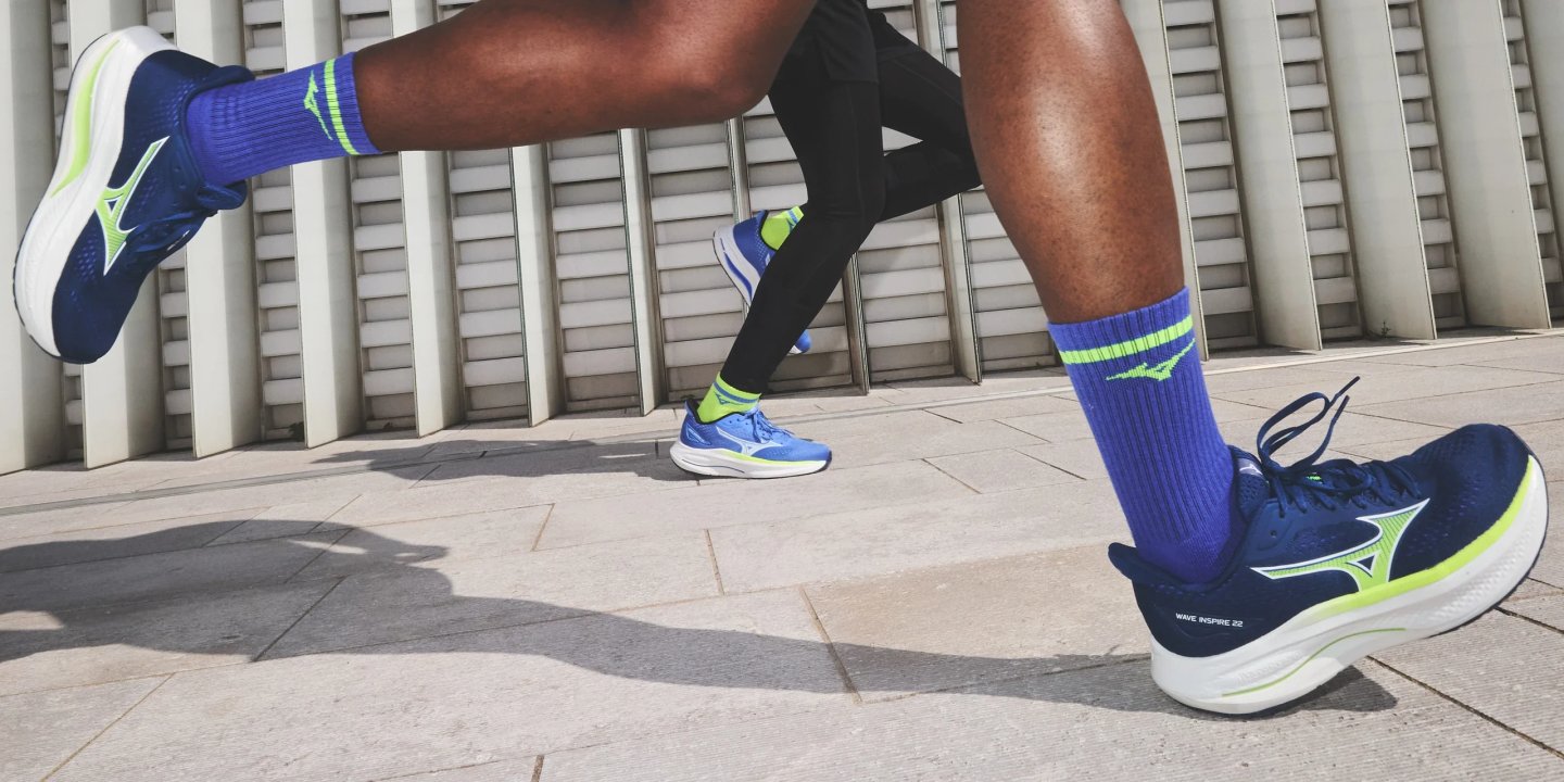 Two runners wearing Mizuno Wave Inspire 22 shoes in navy and neon yellow with matching blue Mizuno crew socks.